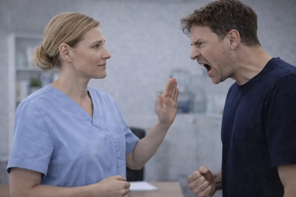 Zorgmedewerker blijft kalm en stelt duidelijke grens wanneer een boze man agressief reageert in een gesprek.