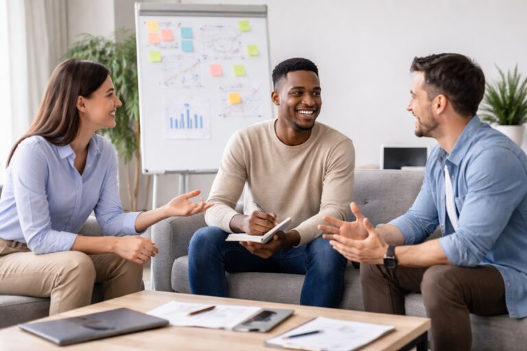 Drie collega’s in een moderne kantoorruimte tijdens een open gesprek, met een ontspannen en professionele sfeer.